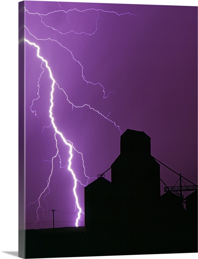 A bolt of lightning lights up the night sky during a storm silhouetting a grain elevator