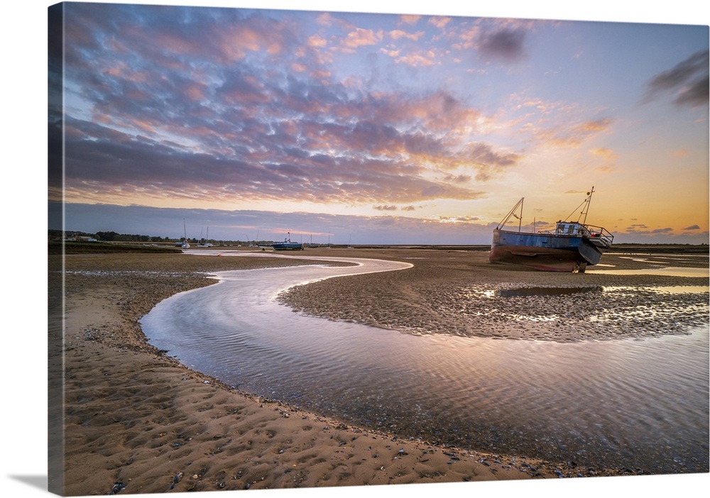 A fishing boat next to a winding river through the sand during sunset at Mow Creek at Brancaster Staithe.