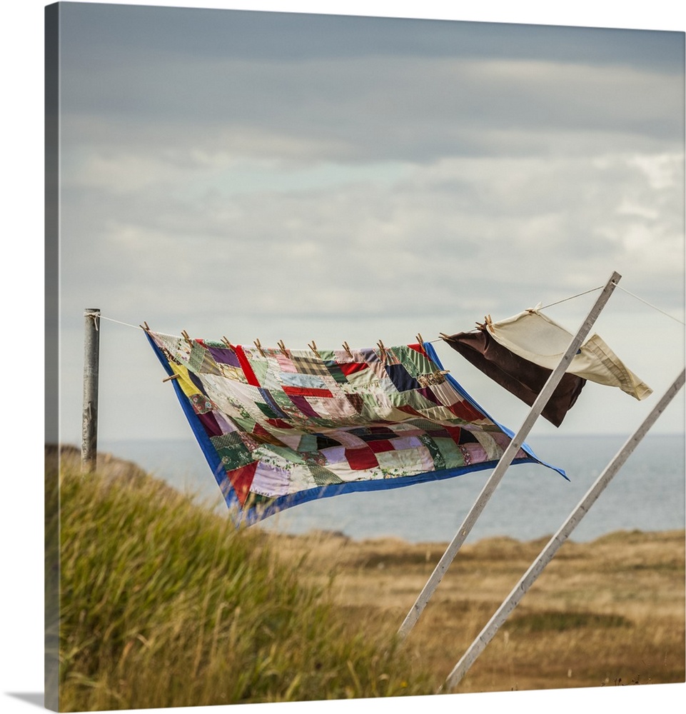 A patchwork blanket and pillow cases hanging on a clothesline with the Atlantic ocean in the background; Newfoundland, Canada