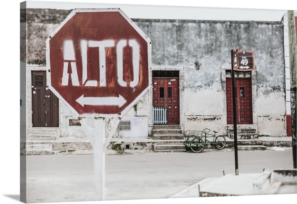 A stop sign with an arrow in Spanish along a street with houses in the background; Cancun, Mexico