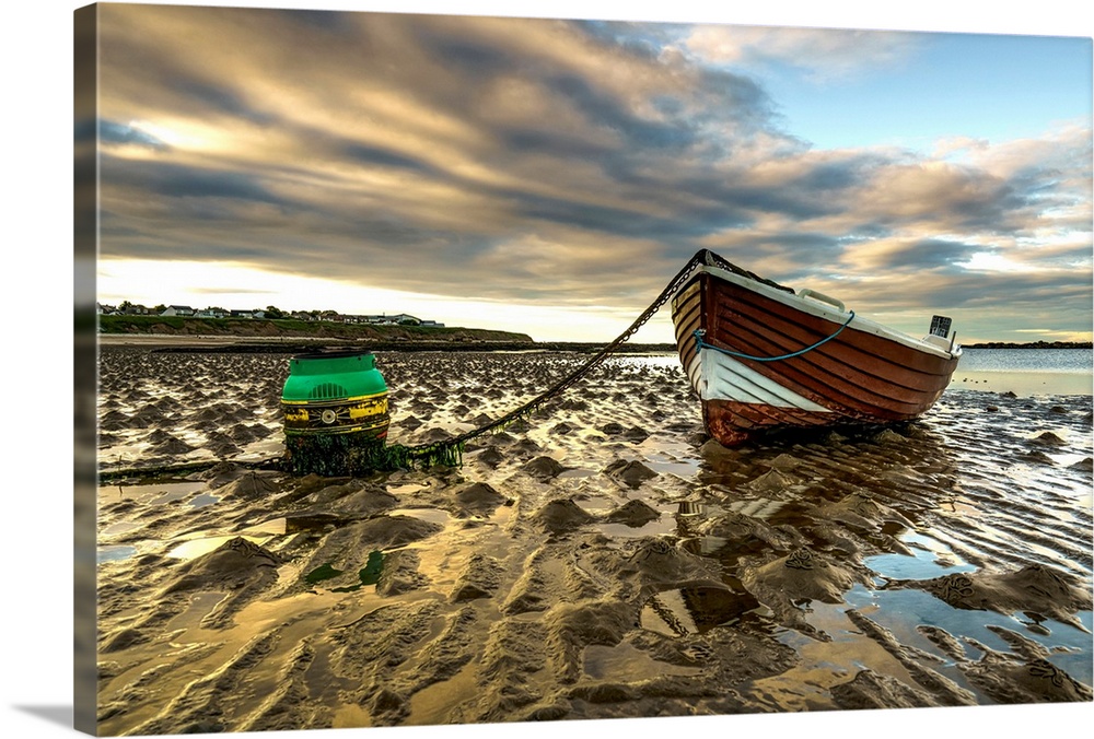 A wooden boat tied to the shore sitting on wet sand at the water's edge at sunset; Whitburn, Tyne and Wear, England