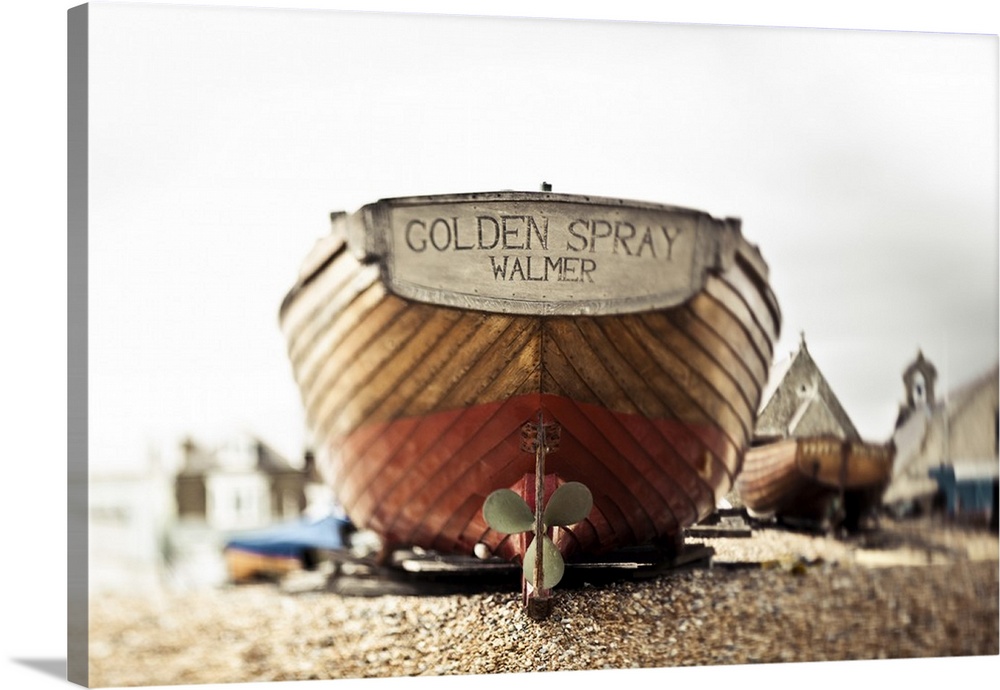 A wooden motorboat sits on the shingle beach with buildings in the background; England