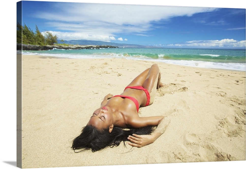 A Young Woman In A Red Bikini Lays On A Sandy Beach; Maui, Hawaii, United States Of America