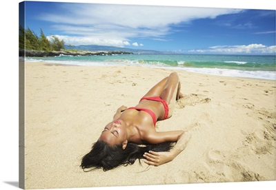 A Young Woman In A Red Bikini Lays On A Sandy Beach; Maui, Hawaii