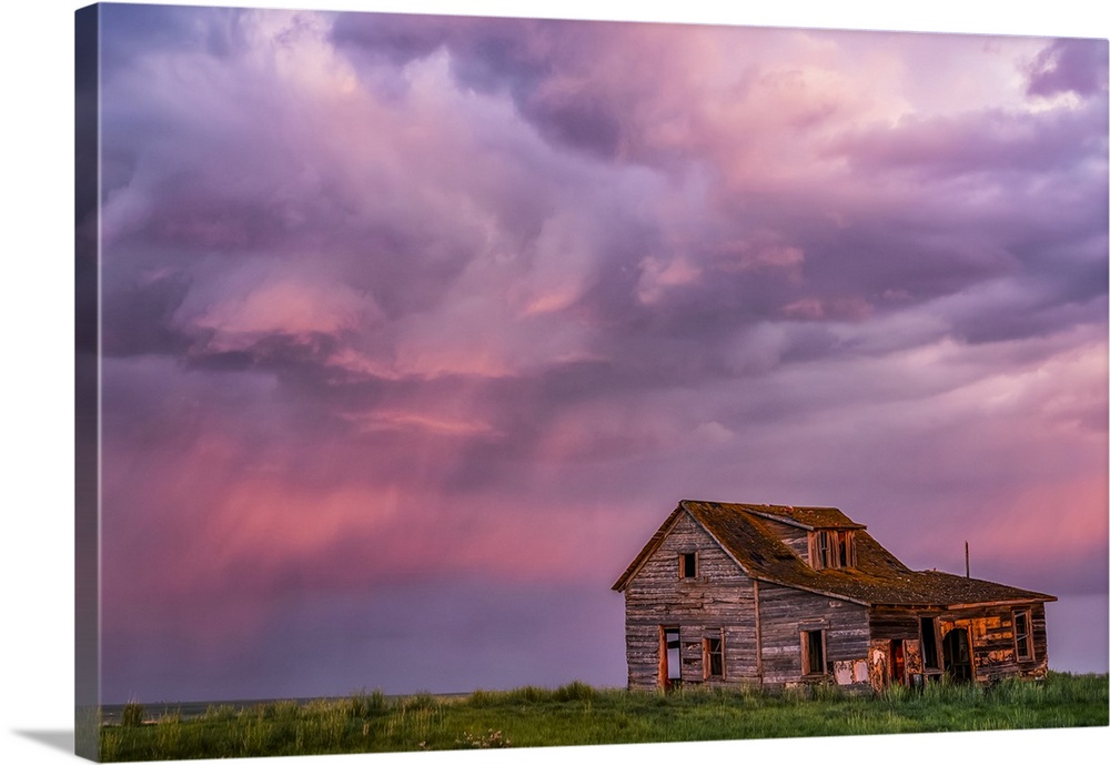 Abandoned barn on farmland with storm clouds glowing pink; Val Marie, Saskatchewan, Canada