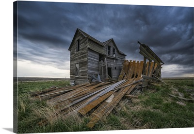 Abandoned house on the prairies with storm clouds overhead at sunset; Val Marie, Canada