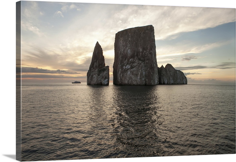An expedition vessel passes near a large rock formation at sunset. Pacific Ocean, Galapagos Islands, Ecuador