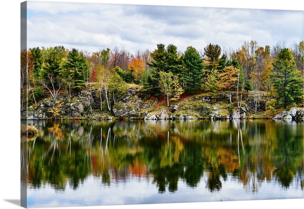 Autumn coloured foliage and clouds in Frontenac Provincial Park reflected in tranquil water; Ontario, Canada