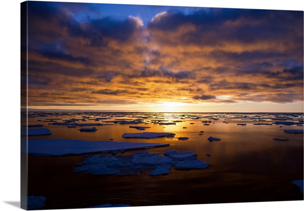 Sunset over pack ice in antarctica, with the bright golden sunlight illuminating the clouds, horizon and reflected on the ...