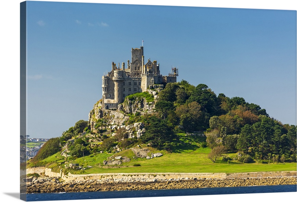 Castle of St. Michael perched on top of a rocky hill along a shoreline, surrounded by trees with blue sky; Cornwall County...