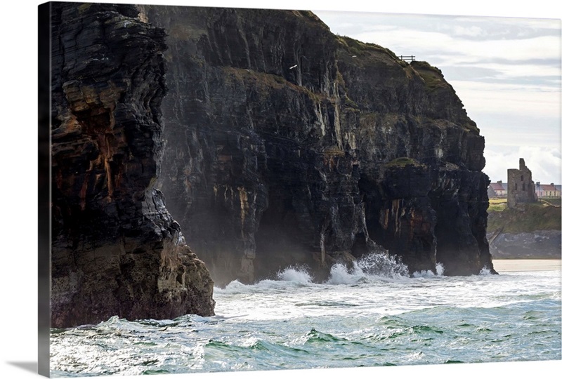 Cliffs with waves crashing into the rock with ruined castle turret ...