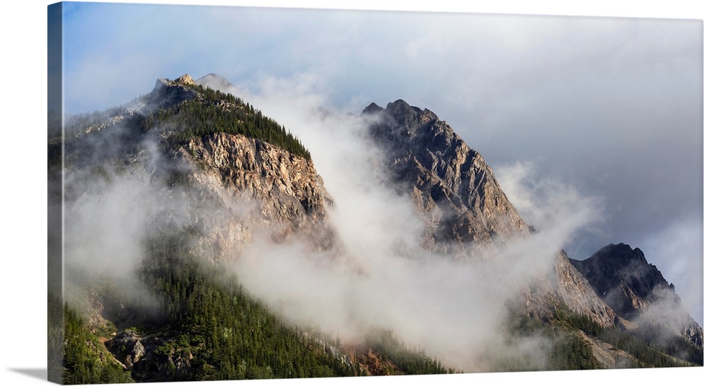 Clouds gather around rocky mountain peaks, field, British Columbia, Canada.