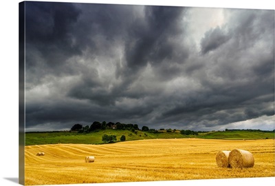 Dark storm clouds roll over a golden farm field with hay bales
