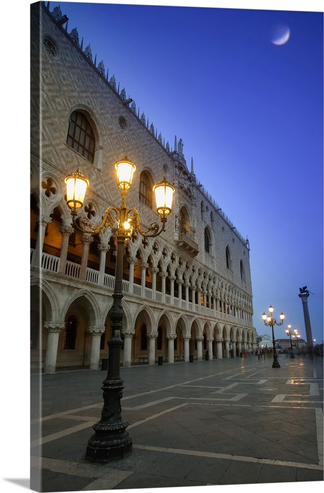 Doge's Palace at dusk with illuminated lamp posts and a moon in the blue sky; Venice, Italy