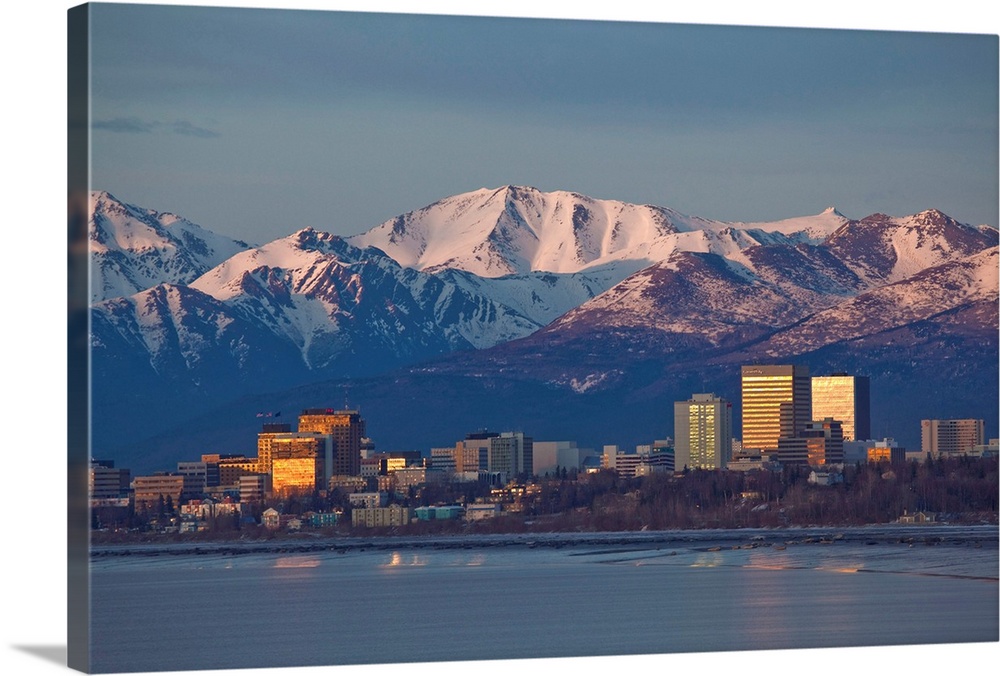 Chugach mountain range seen behind a wide angle view of downtown Anchorage with mudflats in the foreground.