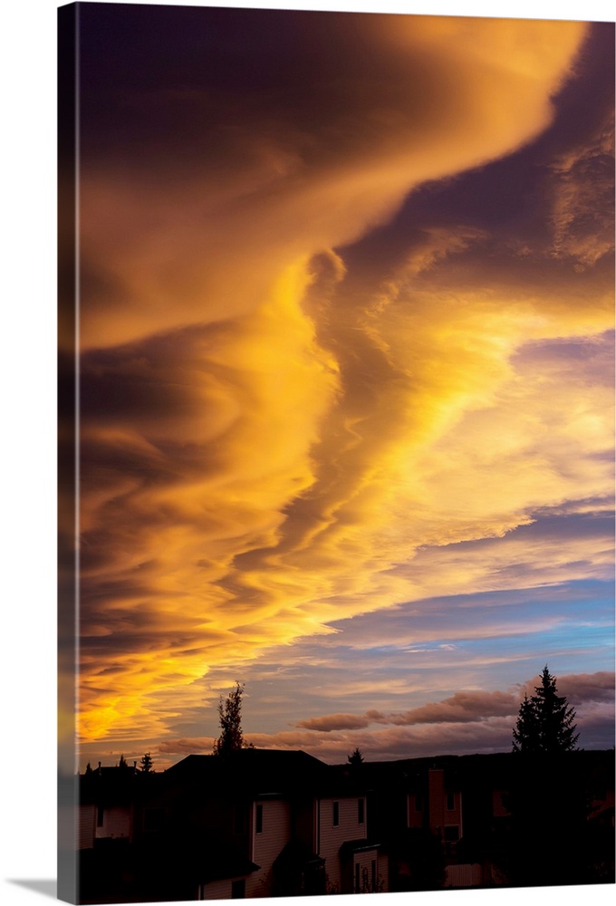 Dramatic colourful clouds at sunset with interesting formations and some blue sky with houses in a neighbourhood. Calgary,...