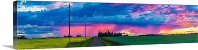 Dramatic colourful sky at sunset over green farmland and a country road; Alberta, Canada