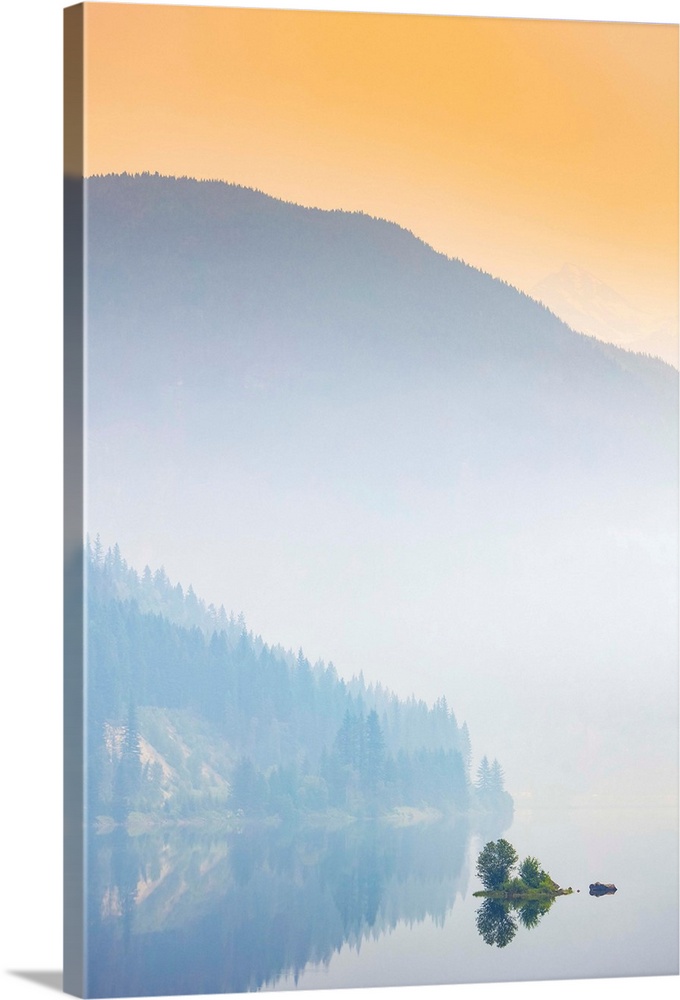 Dense fog over a lake and mountain with a glowing orange sky at sunrise; British Columbia, Canada