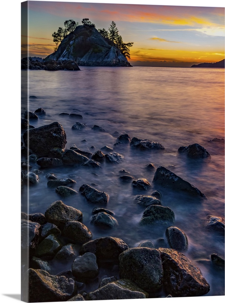 Golden sunlight illuminating the clouds in the distance and wet rocks along the shoreline; Vancouver, British Columbia, Ca...