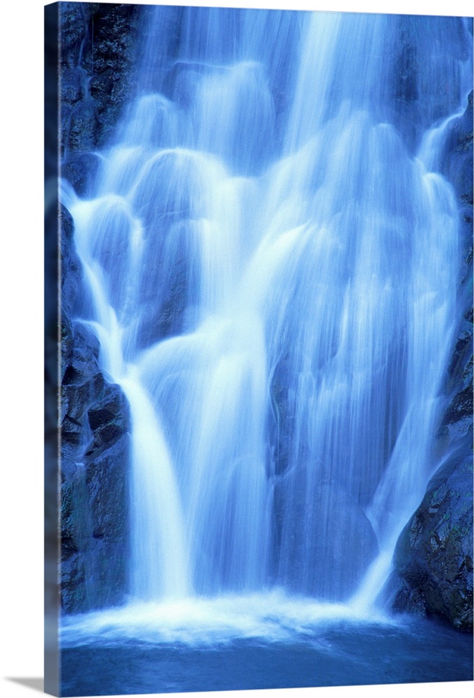 Vertical canvas of a big waterfall rushing down a rocky cliff in Hawaii.