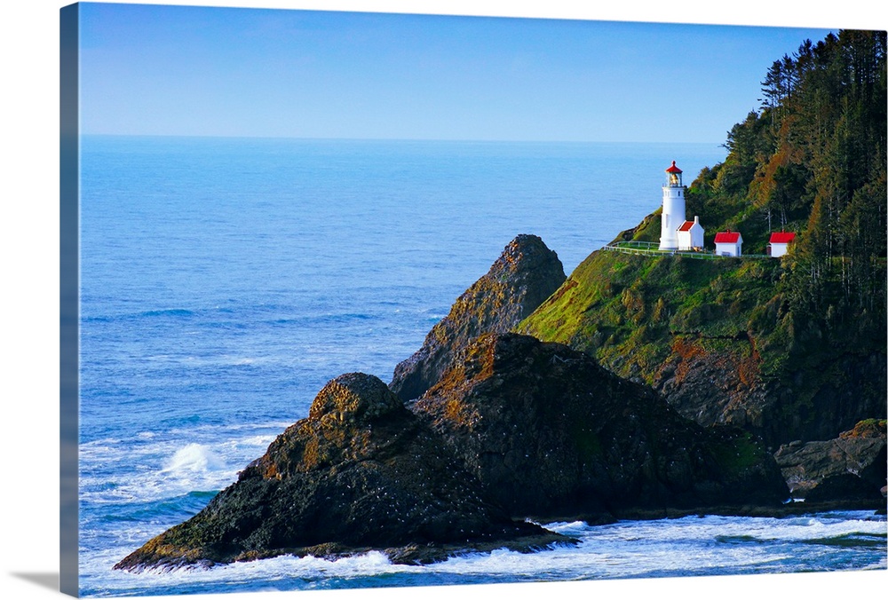 A lighthouse stands on the edge of a cliff that is surrounded by large rock formations in the Pacific ocean.