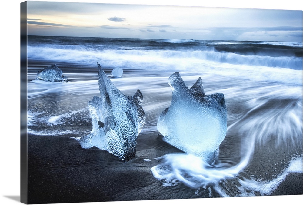 Jagged pieces of broken ice laying on the sandy shore at the edge of the ocean water; Iceland