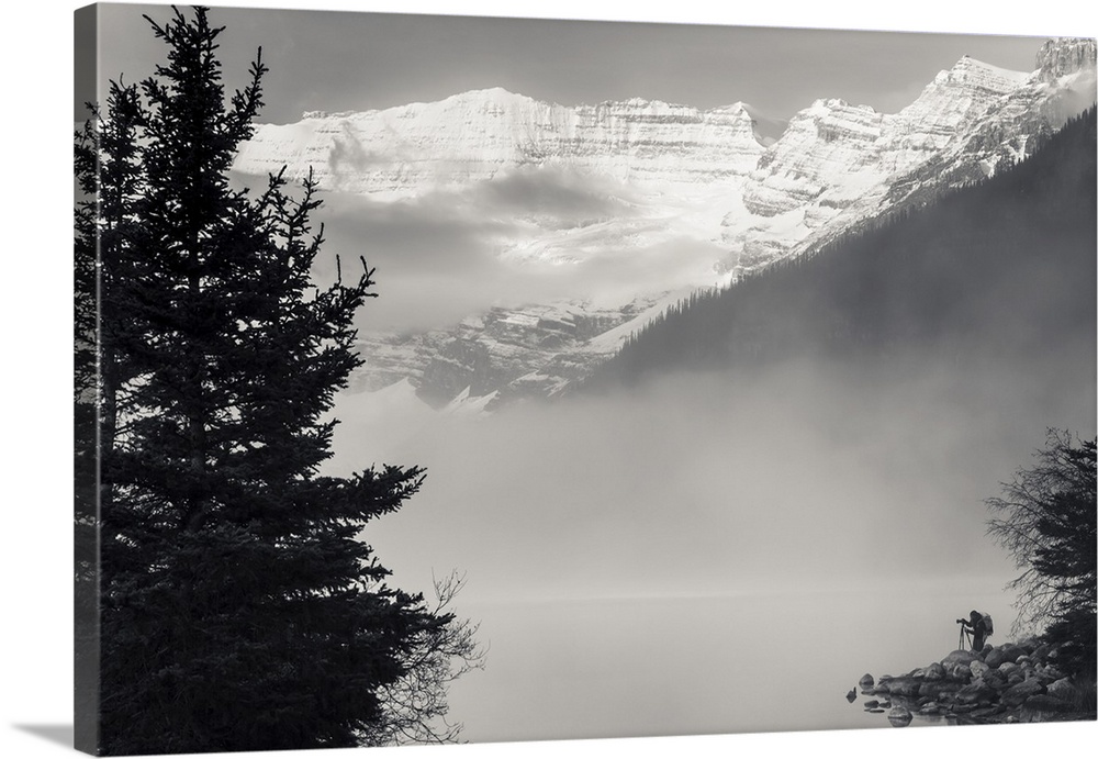 Silhouette of a photographer on the shore of Lake Louise with fog rising from the lake at sunrise, Banff National Park; La...