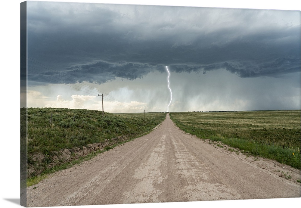 Lightning bolt strikes from a thunderstorm while a lonely road leads into the storm.