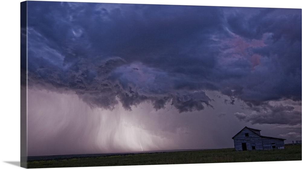 Lightning strikes over the prairies as it approaches an old abandoned farm house; Val Marie, Saskatchewan, Canada
