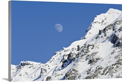 Moon rising over snow covered mountain peak at Hatcher Pass in Southcentral Alaska