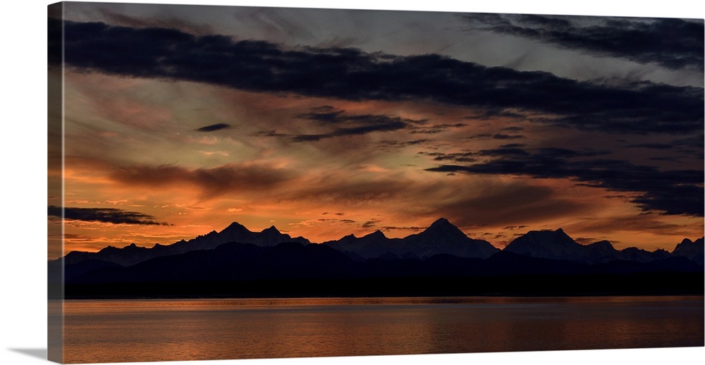 Mountain peaks silhouetted at sunrise, with a dramatic red glowing sky with dark clouds in Glacier Bay National Park and P...