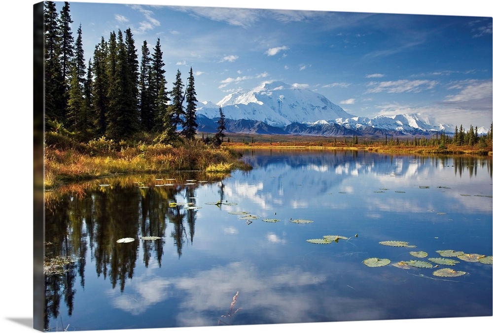 This is a landscape photograph of the Alaskan sky, trees, and mountains mirrored in still waters.