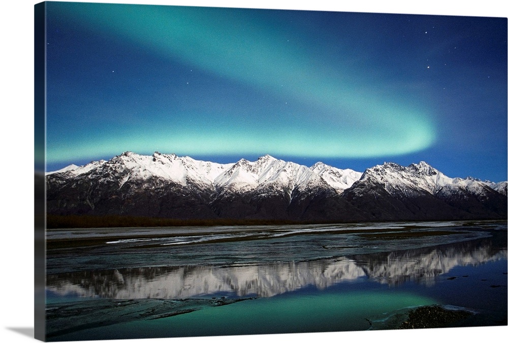 A landscape photograph of the aurora borealis and mountains reflecting in a lake filled with ice.