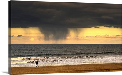 Person and dog walking on the beach under storm clouds, Tyne and Wear, England