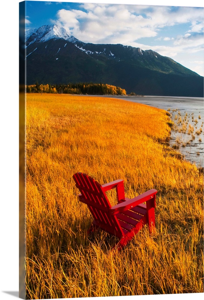 Vertical, large photograph of a single adirondack chair sitting at the edge of a grassy coastline, looking toward the wate...