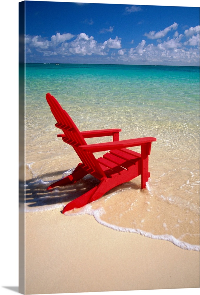 This vertical photograph is taken of a single red beach chair sitting on the edge of the water with a breathtaking view ou...