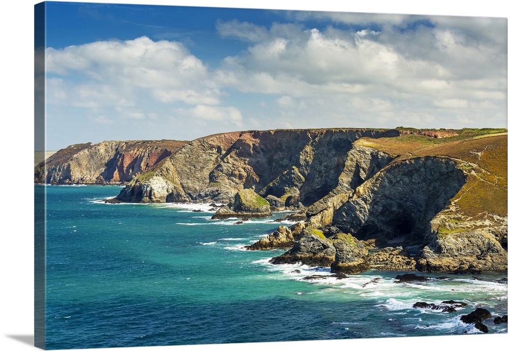 Rocky cliffs along the shoreline with clouds and blue sky; Cornwall County, England.