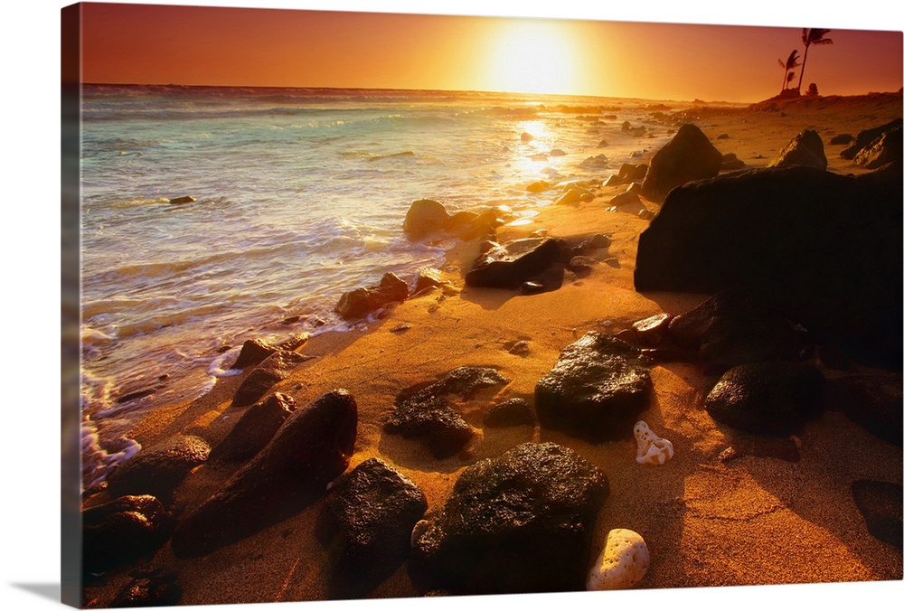 Photograph taken of a sunset on the ocean horizon with various rocks spread out on the beach in the foreground.