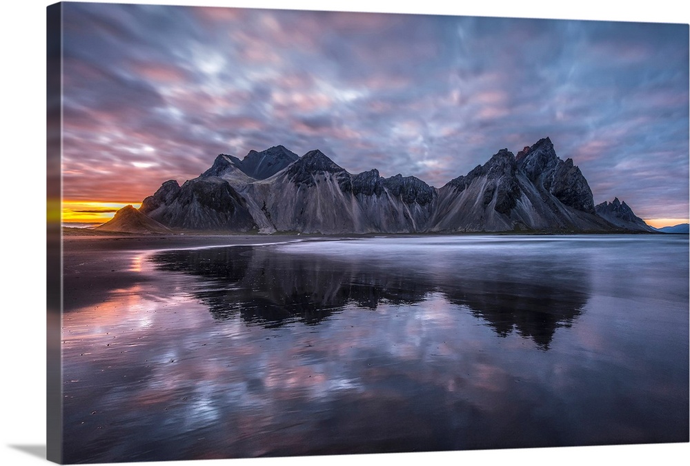 Rugged mountain peaks and a colourful sunset reflected in tranquil water. Iceland.