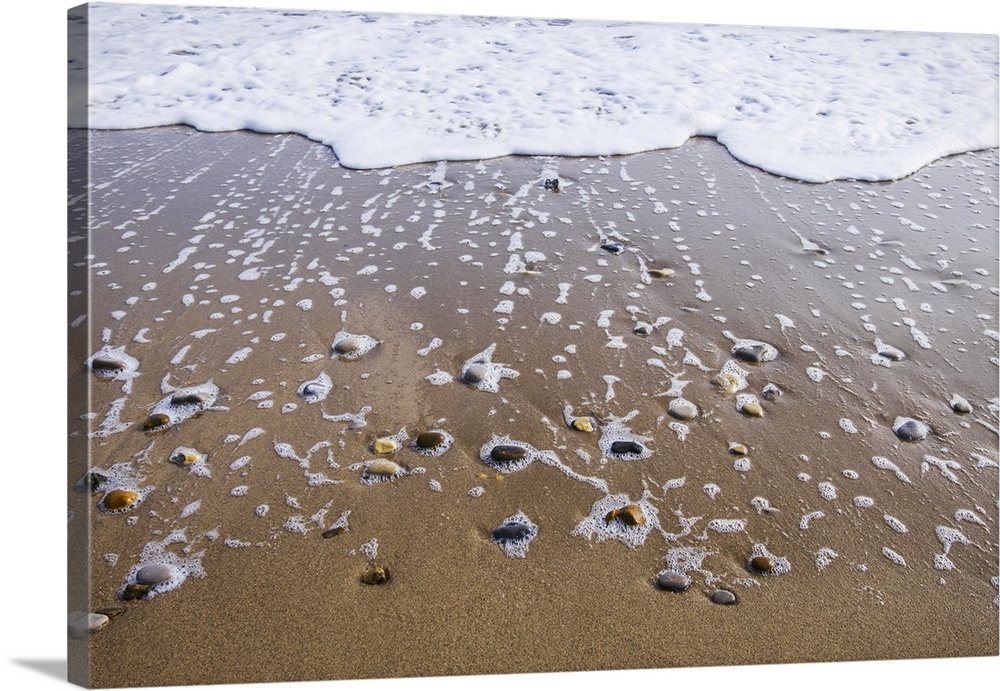 Sea foam trails from beached pebbles as the tide is pulled out, south shields, Tyne and Wear, England.