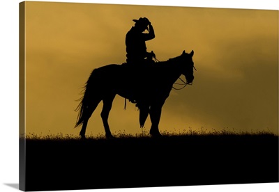 Silhouette Of A Cowboy On A Horse Against A Sky Of Golden Cloud At Sunset, Montana