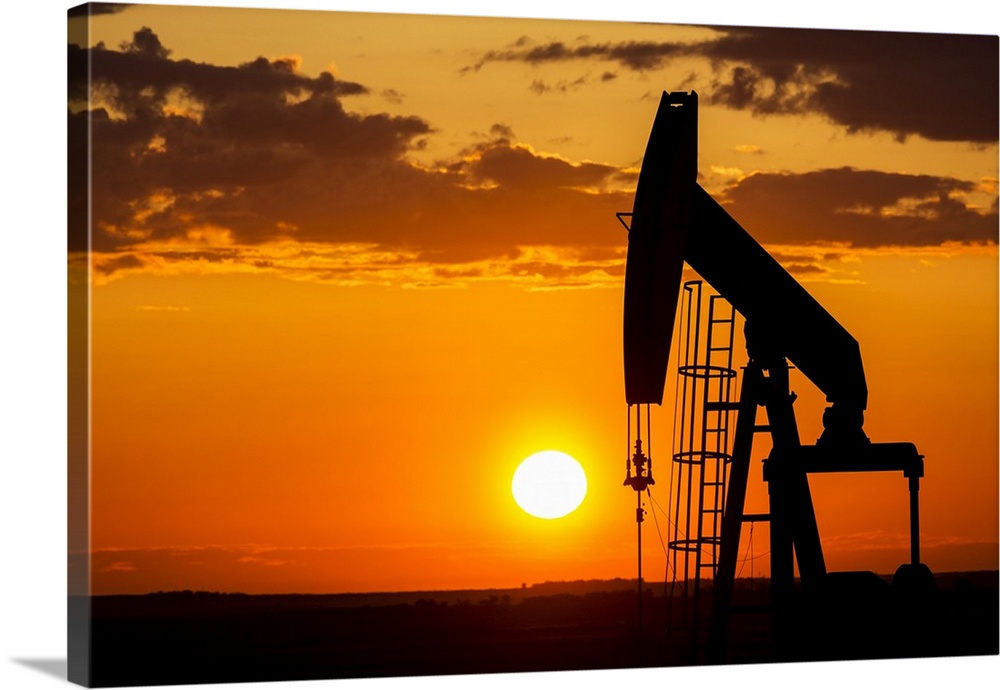 Silhouette Of A Pump Jack At Sunrise With A Colorful Orange Sun, Clouds And Sky; Alberta, Canada