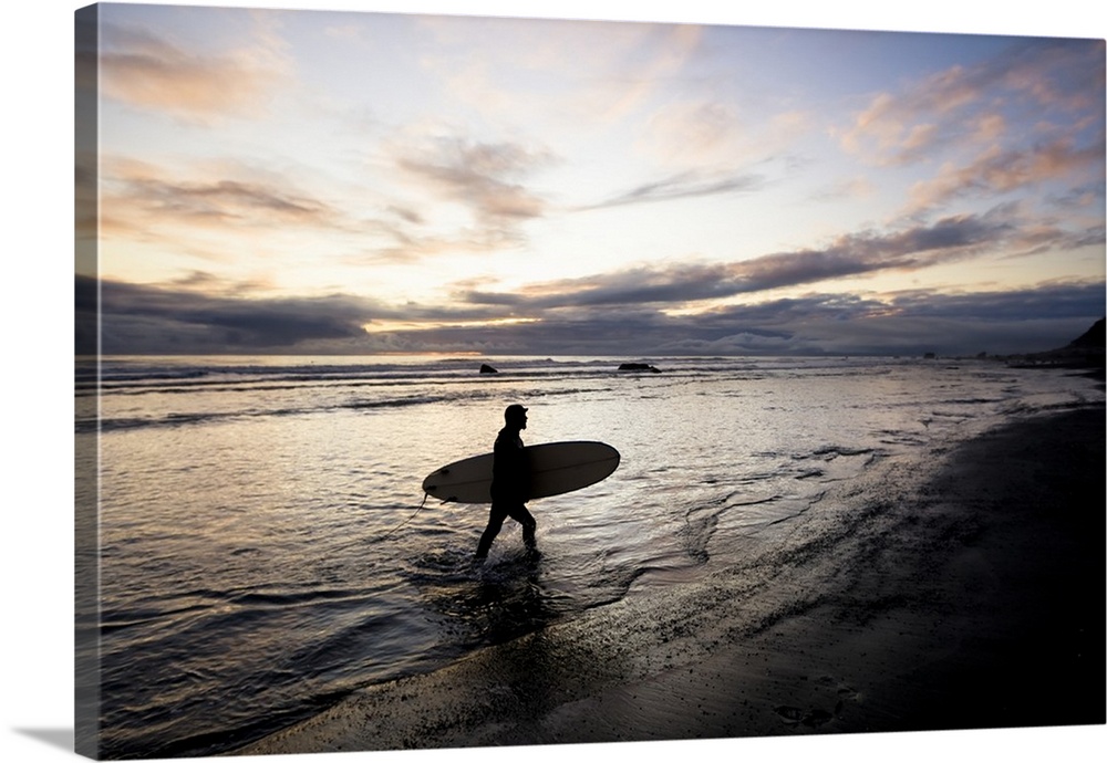 Silhouette Of A Surfer Carrying A Surfboard Back To Shore At Sunset; Alaska, United States Of America