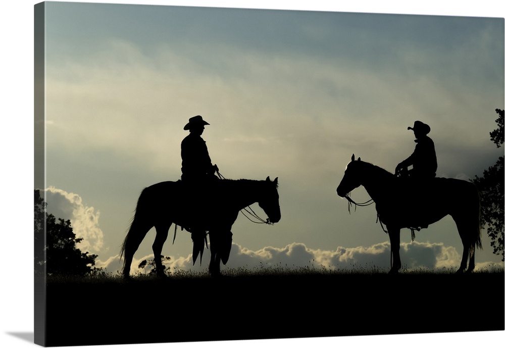 Silhouette of two cowboys on horses against a cloudy sky; Montana, United States of America.