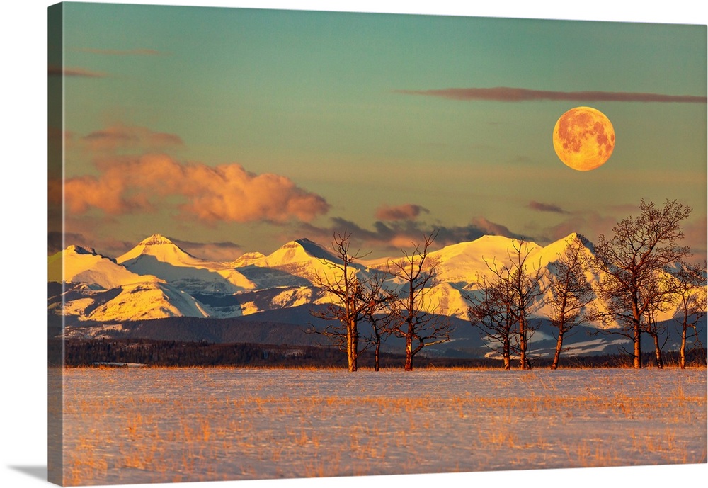 Snow-covered mountain range reflecting warm light at sunrise with a warm glowing full moon, clouds in a blue sky, and a sn...