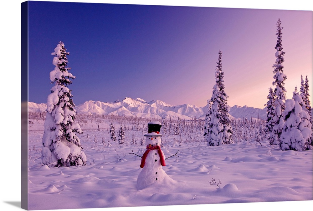 Large canvas photo of a snowman sitting in a snowy landscape with mountains in the distance and snow covered trees surroun...