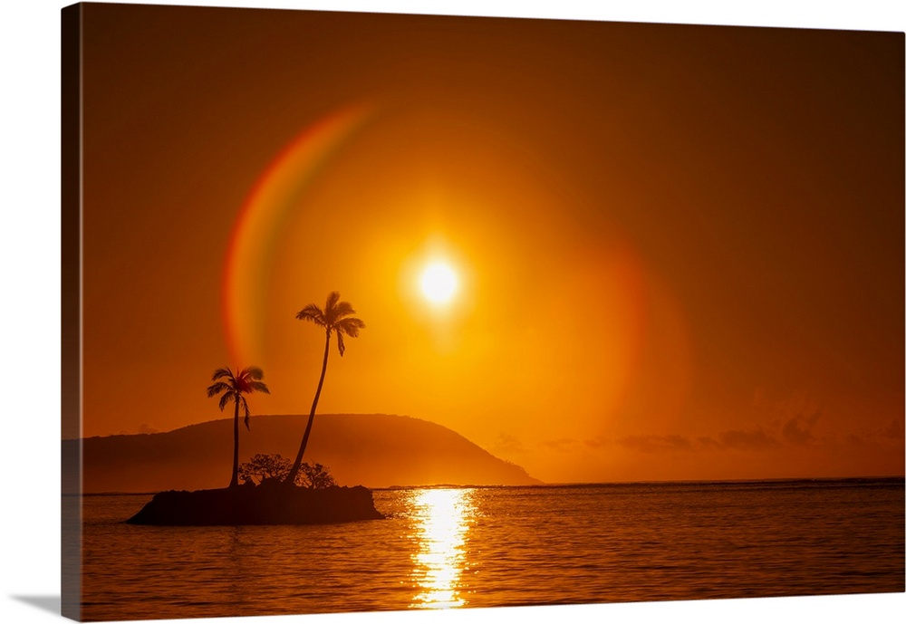 Sunrise at Kahala Beach, Waialae Beach Park, with a flare around the sun in a glowing red sky reflected in the tranquil wa...
