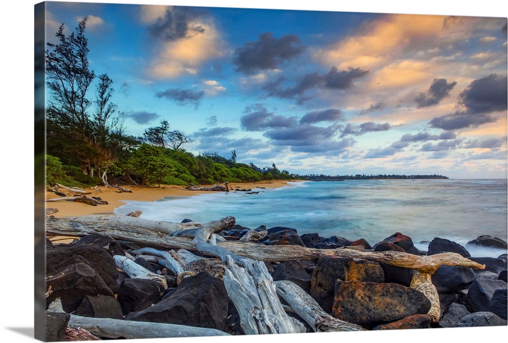 Sunrise over Lydgate beach and ocean with rocks and driftwood in the foreground and the coastline in the distance; Kapaa, ...
