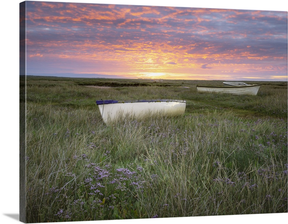 Sunrise over small boats on the salt marsh surrounded by sea lavender.