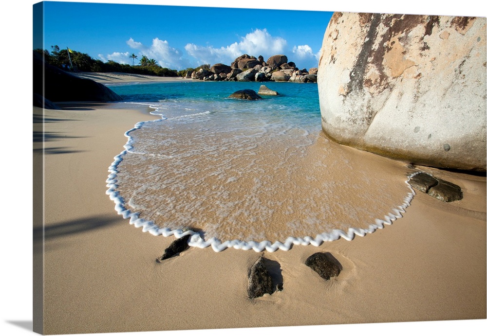 Stunning view of the sandy beach with surf forming a zigzag pattern in the foam next to the large, boulders lining the sho...